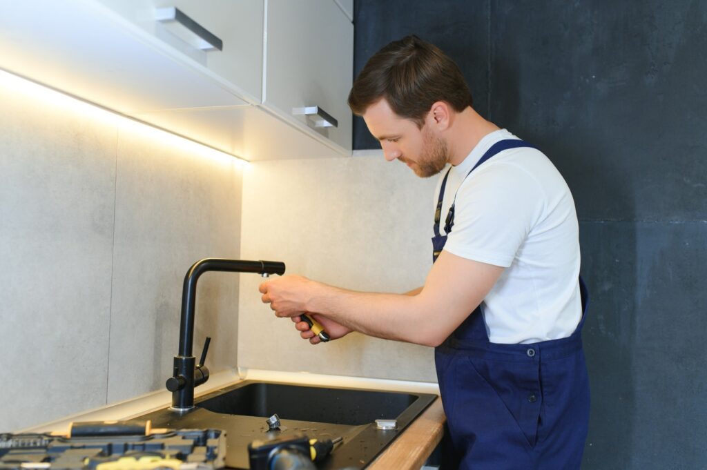 A handyman fixing a leaky faucet to prevent water damage in a home.