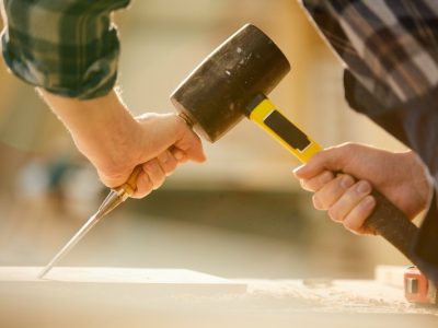 A carpenter holding a hammer and screwdriver while working on a furniture
